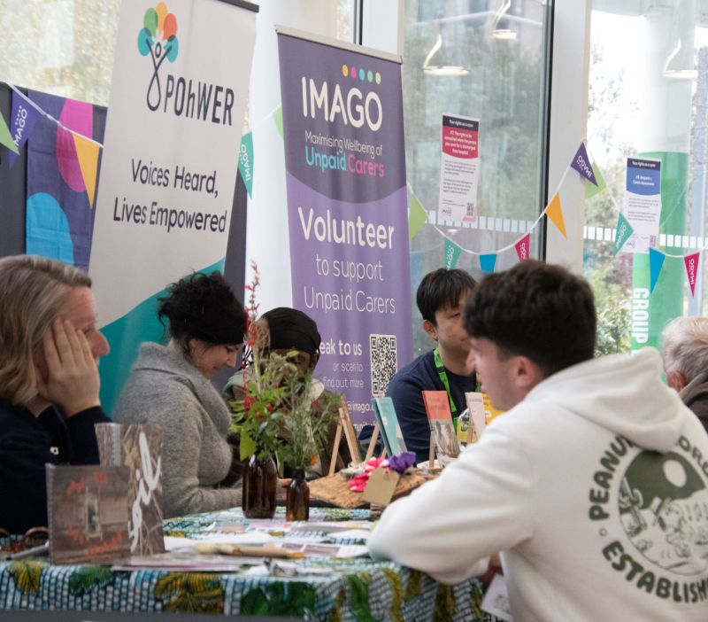 poeple chatting at an information event. Stall holders visible include Pohwer and Imago